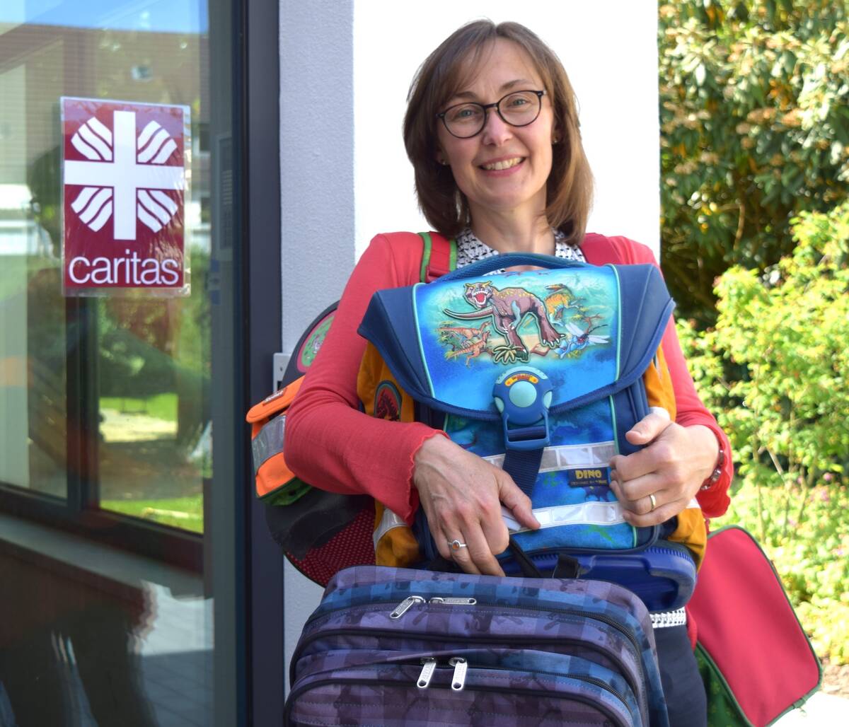 Maria Weiss von der Caritas hält und zeigt mehrere gespendete Schulranzen und Schultaschen.
