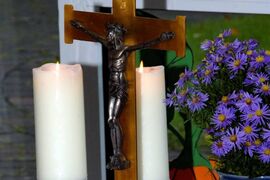 Ein Kruzifix, zwei Kerzen und Blumen auf einem Tisch.