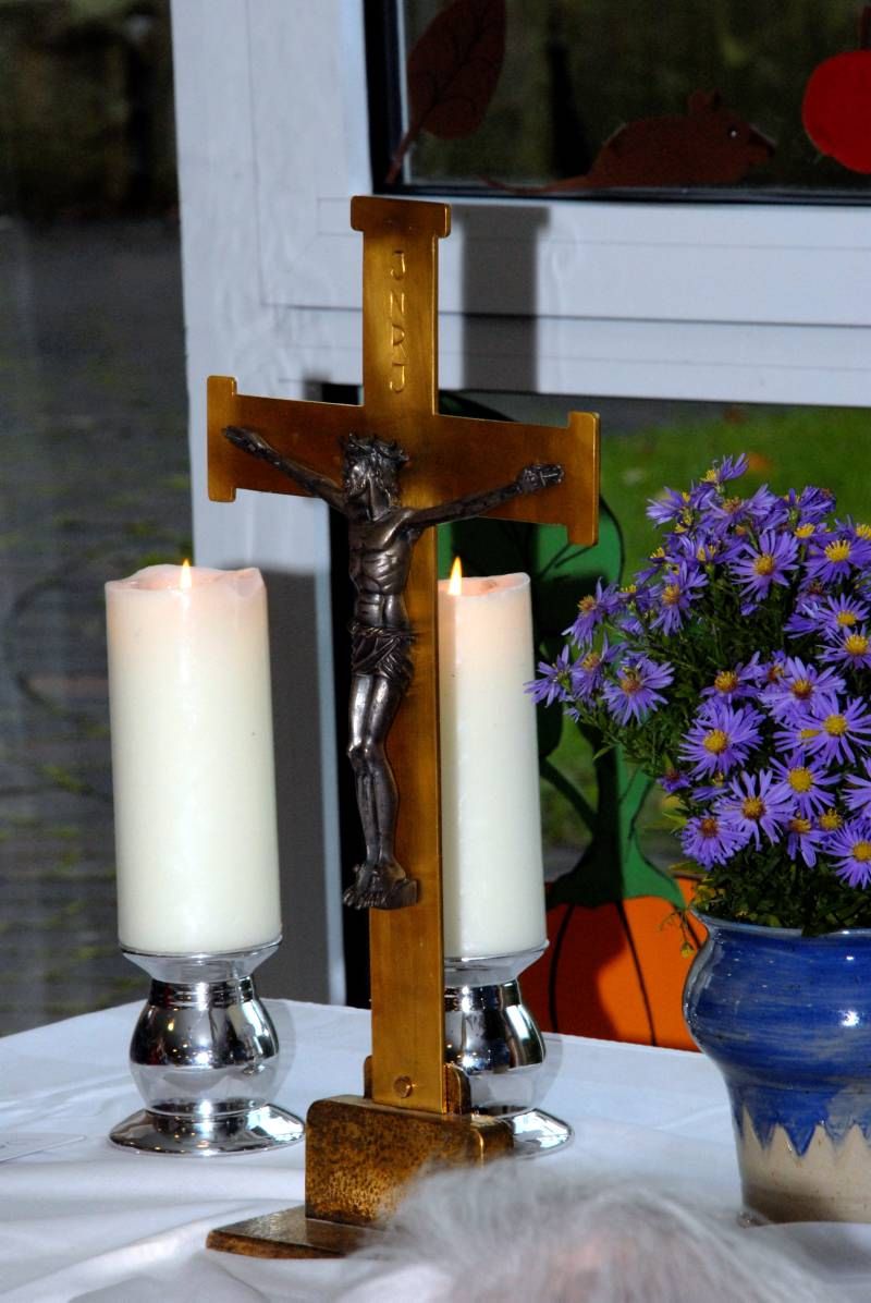 Ein Kruzifix, zwei Kerzen und Blumen auf einem Tisch.